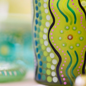 Close-up of a brightly painted artwork featuring green, blue, and pink dot patterns in an Aboriginal style.